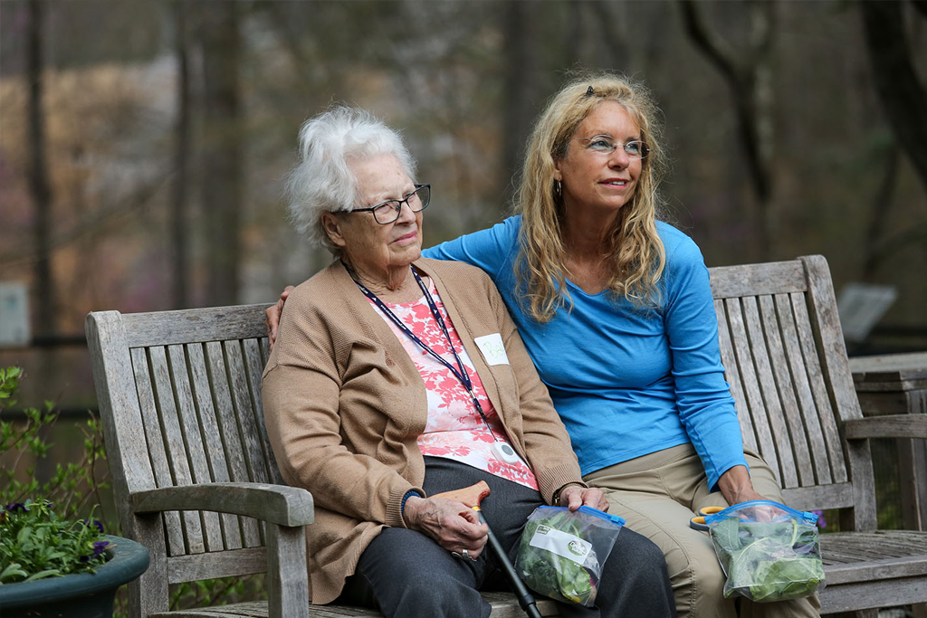 Elderly woman and caregiver sitting on a park bench