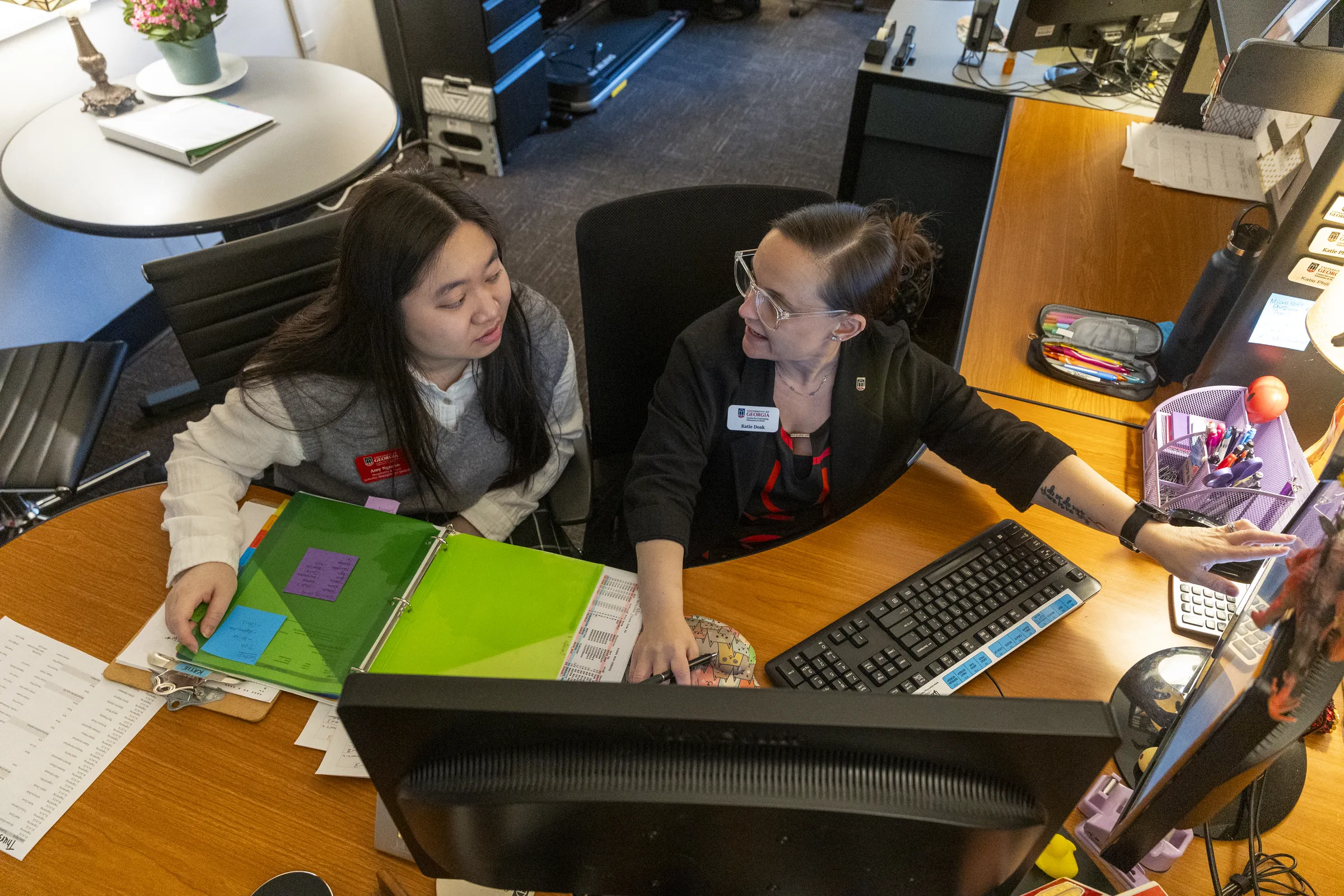 Two women sit at a desk in an office at the Georgia Center. They are dressed professionally and looking at a computer screen.