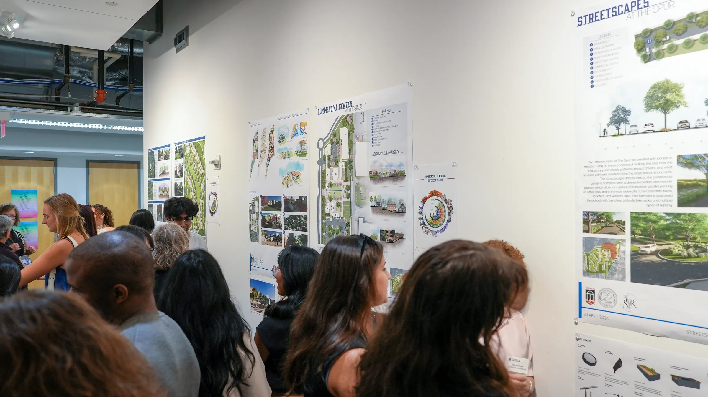 Several students observe city planning documents that are posted on a white wall.