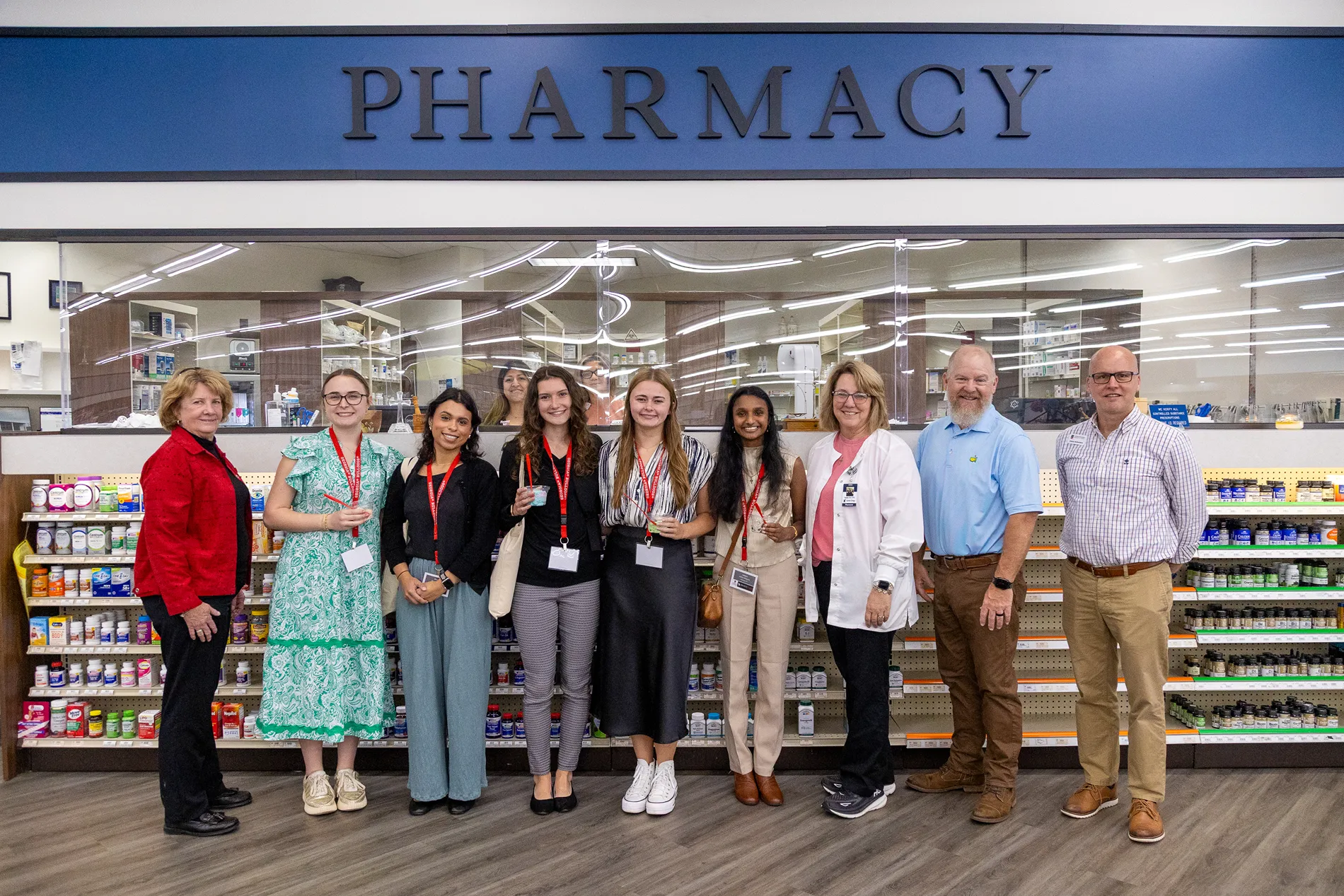 A group of medical professionals and students pose outside of a pharmacy.