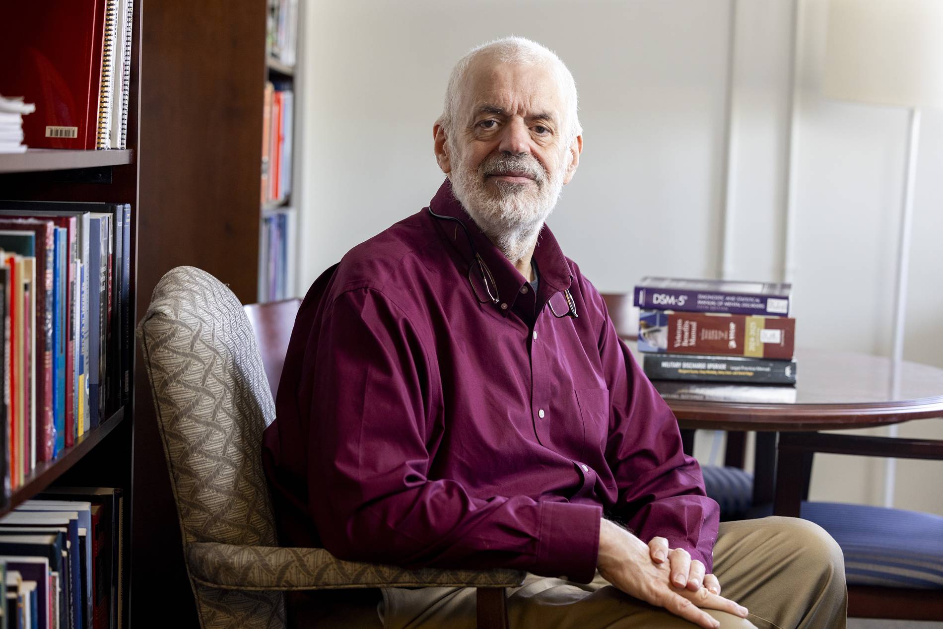 An older man in a red collared shirt sits in a chair.